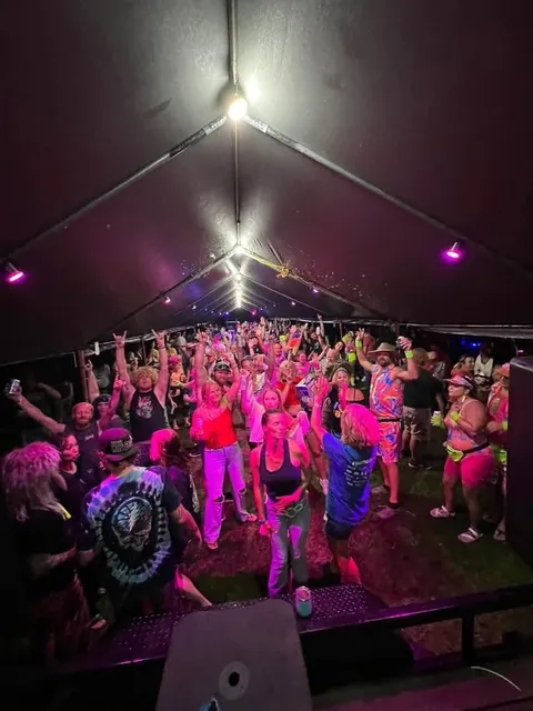 A crowd dancing under neon pink and purple lights inside the themed tent party